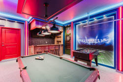 Enter a lively game room with a sleek pool table lit by colorful LEDs, enhancing the energetic vibe. The bold red door and sports-themed decor promise unforgettable moments with friends and family.