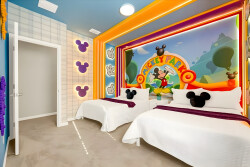 Brightly colored walls feature a playful mural, making this room a delightful escape for families. With two cozy beds adorned in crisp white linens and soft purple accents, this vibrant space is designed for fun and comfort.
