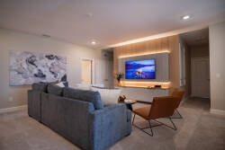 Unwind in the stylish living room on a plush gray sectional, basking in the soft glow of ambient lighting. Enjoy the sleek television framed by warm wood accents and contemporary wall art that adds personality to your space.