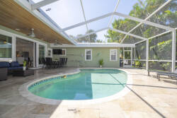 Relax in your private oasis featuring a sparkling pool in a sleek screened enclosure, perfect for sunbathing. The natural stone patio and lush greenery create a serene setting for your relaxation and gatherings.