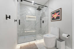 Experience the elegance of this beautifully designed bathroom, complete with a spacious glass shower and sleek black fixtures. The sophisticated marble tiles and vibrant floral artwork bring personality to your daily routine.