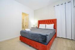 Relax in this stylish bedroom featuring a bold, red tufted bed that stands out against the crisp white walls. Natural light floods the space through elegant curtains, creating a warm atmosphere for restful nights.