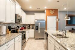 Cook with ease in a bright fully equipped kitchen with white cabinets, granite countertops, stainless steel appliances, pendant lights, and a spacious island perfect for family meals.