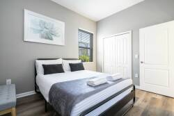 Welcome to a bright bedroom featuring a comfy bed with stylish gray linens and decorative pillows, perfect for relaxation. Natural light fills the space, highlighting soft decor tones and creating a cozy, inviting atmosphere.