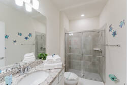 This bright bathroom features a sleek glass shower and spacious granite countertop, ideal for morning routines. Cheerful blue accents add a playful touch, while plush towels and greenery create a refreshing atmosphere.