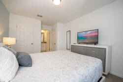 Experience a cozy bedroom with soft blue accents and a plush queen bed dressed in elegant linens. A sleek dresser provides storage, while a flat-screen TV and a stylish lamp create a warm, inviting atmosphere for relaxation.