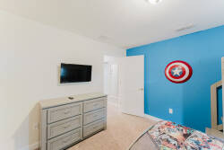 This bright and playful guest room boasts a vibrant blue accent wall and soft beige carpeting, creating a welcoming atmosphere. Enjoy ample storage with a stylish dresser and easy entertainment with a wall-mounted TV.