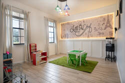 Welcome to our vibrant playroom, featuring a lively green rug and colorful pendant lights. With a charming play kitchen and playful decor, it's the perfect space for your little ones to explore their creativity and laughter.