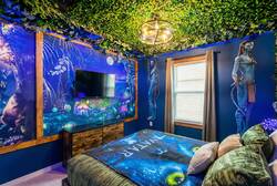 Rest in an Avatar themed bedroom with a cozy bed, blue walls, leafy ceiling, glowing lights, bold wall art, and bow-and-arrow decor, creating a fun space for vacation.