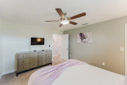 Unwind in this airy bedroom with a plush bed and soft linens, complemented by a stylish ceiling fan for comfort. The light green walls and modern dresser add contemporary charm, creating a soothing retreat for your stay.