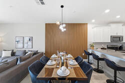 Gather in a bright dining area with a set wooden table, cozy blue chairs, modern globe lighting, warm wood accent wall, bar seating, and open access to the kitchen.