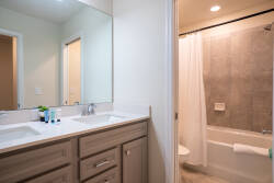 Experience a beautifully designed bathroom with a spacious double vanity, sleek wood cabinetry, and a large mirror that brightens the space. Enjoy the calming gray tiles and well-equipped shower for a refreshing stay.