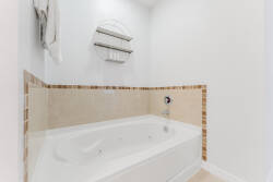 Relax in a beautifully tiled corner featuring a spacious jetted tub surrounded by warm earth tones. The crisp white walls and soft lighting create a soothing atmosphere, ideal for a refreshing soak after a long day.