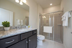 Experience the elegance of this well-appointed bathroom, featuring a sleek granite countertop and dark cabinetry. Enjoy refreshing moments in the glass-enclosed shower, all illuminated by warm, inviting lighting.