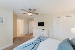 This cozy bedroom, with its soft neutral tones and plush blue throw, creates a tranquil atmosphere. Enjoy the modern ceiling fan, wall-mounted TV for convenience, and spacious closets for all your storage needs.