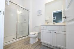 This bright bathroom showcases modern fixtures and a spacious glass shower for refreshing moments. With warm wooden flooring and crisp white cabinetry, it creates a clean, airy atmosphere ideal for your stay.