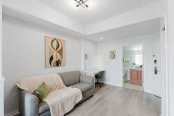 Relax in this cozy living area, featuring a sleek gray sofa with a soft throw and vibrant artwork on light walls. A green chair in the workspace invites productivity, and the open layout connects effortlessly to other spaces.