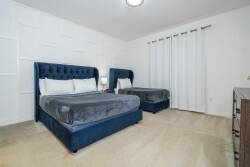 Experience tranquility in a soothing bedroom with plush deep blue beds and soft neutral walls, enhanced by natural light streaming through white drapes. This elegant design ensures a cozy atmosphere for restful nights.