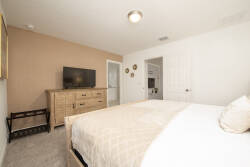 This cozy bedroom features a plush bed with soft linens, complemented by warm beige accents and a stylish wooden dresser. The room is brightened by natural light, creating a peaceful atmosphere for a restful stay.