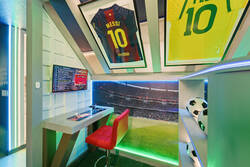 Enjoy a soccer themed gaming nook with framed jerseys, stadium wall art, arcade controls, LED lighting, soccer ball decor, and a colorful seat, creating a fun space for vacation entertainment.