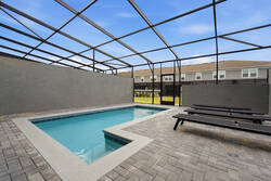 Relax in a private screened pool area with clear blue water, lounge chairs, paved deck, privacy walls, and open sky views, creating a refreshing space for family vacation moments.