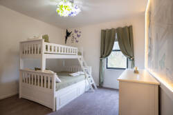 This bright and cheerful room features a charming white bunk bed ideal for families, with cozy green bedding and soft plush carpet. Whimsical drapes and a playful ceiling fixture enhance the inviting atmosphere for your stay.
