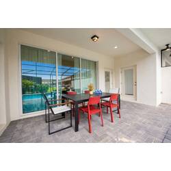 Enjoy outdoor meals on a covered patio with a black dining table, red chairs, sliding glass doors, pool view, and paved flooring, creating a relaxed space for vacation moments.