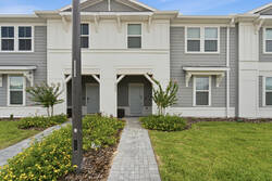 Arrive at a charming modern townhouse with a clean gray and white facade, paved walkway, green lawn, landscaped garden, and covered entry, creating a welcoming start to your vacation.