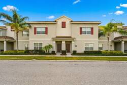Arrive at a welcoming two-story townhome with a bright exterior, red shutters, palm trees, and fresh landscaping. A calm street view and clean façade create a pleasant first impression for your Florida vacation.
