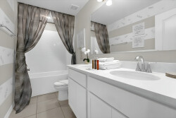 Welcome to your beautifully designed bathroom, featuring a sleek white vanity and elegant marble accents. Enjoy the calming atmosphere created by soft striped wallpaper, flowing curtains, and fresh towels for your comfort.