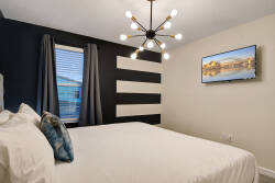 This stylish bedroom boasts a cozy white bed with decorative pillows and a striking black-and-white accent wall. A modern light fixture adds a contemporary touch, while the window invites natural light to create a warm atmosphere.