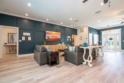 This spacious living area boasts a striking blue accent wall and chic wood flooring, offering a contemporary feel. Unwind on the modern gray sectional, bask in the natural light from large windows, and gather around the unique.