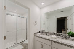 Experience a bright, stylish bathroom with sleek white cabinetry and a spacious granite countertop that enhances the glass shower. Abundant lighting and mirrors create an airy atmosphere, making your daily routine refreshing.