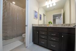 Experience a sleek bathroom with a spacious granite countertop and elegant wooden cabinetry for your essentials. Soft, natural light highlights modern fixtures and decor, creating a refreshing and inviting atmosphere.