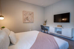 Relax in this cozy bedroom with soft greys and blush tones. The plush bed with decorative pillows invites comfort, while the wall-mounted TV is perfect for movie nights. A stylish desk chair adds a great touch for quiet moments.