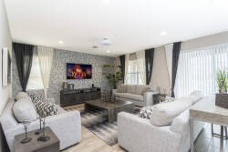 Welcome to a bright living area with soft gray sofas and a stylish accent wall. Large windows dressed in elegant curtains let in natural light, creating an airy space for you to unwind after a day of adventure.