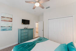 This bright and airy bedroom offers a cozy queen bed with crisp white linens and a vibrant teal throw. Enjoy the contemporary dresser, wall-mounted TV, and a ceiling fan that adds to the relaxed atmosphere for your stay.