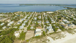 Embrace the beauty of coastal living with breathtaking aerial views of charming homes surrounded by lush greenery and sandy shores. Relax by the tranquil water just steps away, inviting you to unwind and explore.