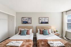 Rest in a bright bedroom with two cozy beds, soft pillows, warm blankets, abstract wall art, natural light, and clean neutral tones, creating a comfortable space for your vacation.