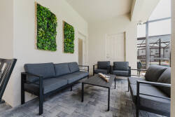 Welcome to the stylish lounge, where a sleek black metal frame sofa and cozy armchairs invite you to relax. The textured gray pavers and vibrant green wall art create a fresh and comfortable atmosphere for your enjoyment.
