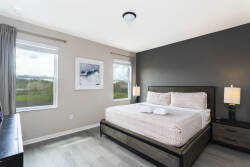 Experience serenity in this beautifully designed bedroom, featuring a plush queen-size bed with crisp linens, stylish lamps, and large windows that fill the space with natural light and offer stunning views.