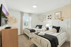 This cozy bedroom, filled with natural light, features two twin beds dressed in crisp white linens and stylish black accents. Subtle coastal decor and soft textures add to the inviting atmosphere, perfect for a relaxing stay.