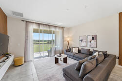 Relax in a bright living room with cozy gray seating, a wall-mounted TV, warm wood accent wall, soft curtains, modern decor, and sliding glass doors opening to a peaceful balcony view.