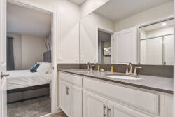 This sleek bathroom boasts a spacious double vanity with stylish fixtures and a clean, neutral color palette that enhances the bright lighting, while the adjoining bedroom offers a tranquil sleeping area ideal for unwinding.