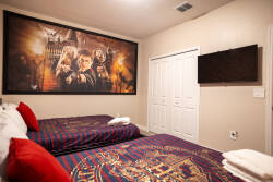 This vibrant bedroom offers two cozy beds with rich blue and gold patterns and plush red throw pillows. A captivating mural adds character, and the flat-screen TV ensures entertainment is always at your fingertips.