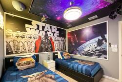 Rest in a Star Wars themed bedroom with two cozy twin beds, galaxy ceiling, neon sign, space decor, dark curtains, and bold wall art, creating an exciting space for kids during vacation.