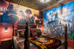 Rest in a magical wizard themed bedroom with a cozy four poster bed, castle wall murals, warm lighting, rich colors, and detailed ceiling decor, creating a fun and immersive vacation space.