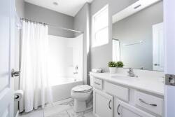 This bright, airy bathroom showcases a sleek white vanity on soft gray walls, creating a refreshing ambiance. Natural light fills the space, enhancing the clean lines of the tiled floor and inviting a serene atmosphere.