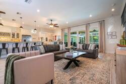 Welcome to a bright, spacious living area filled with natural light from large sliding doors. Cozy gray sofas and a textured rug create a warm atmosphere, seamlessly flowing into a stylish kitchen perfect for entertaining guests.