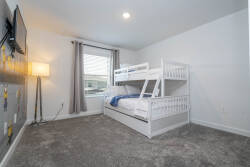 This bright bedroom features a cozy bunk bed, perfect for kids or extra guests, while soft gray carpeting adds warmth. The large window invites natural light, enhancing the airy feel, and the playful wall decor sparks imagination.